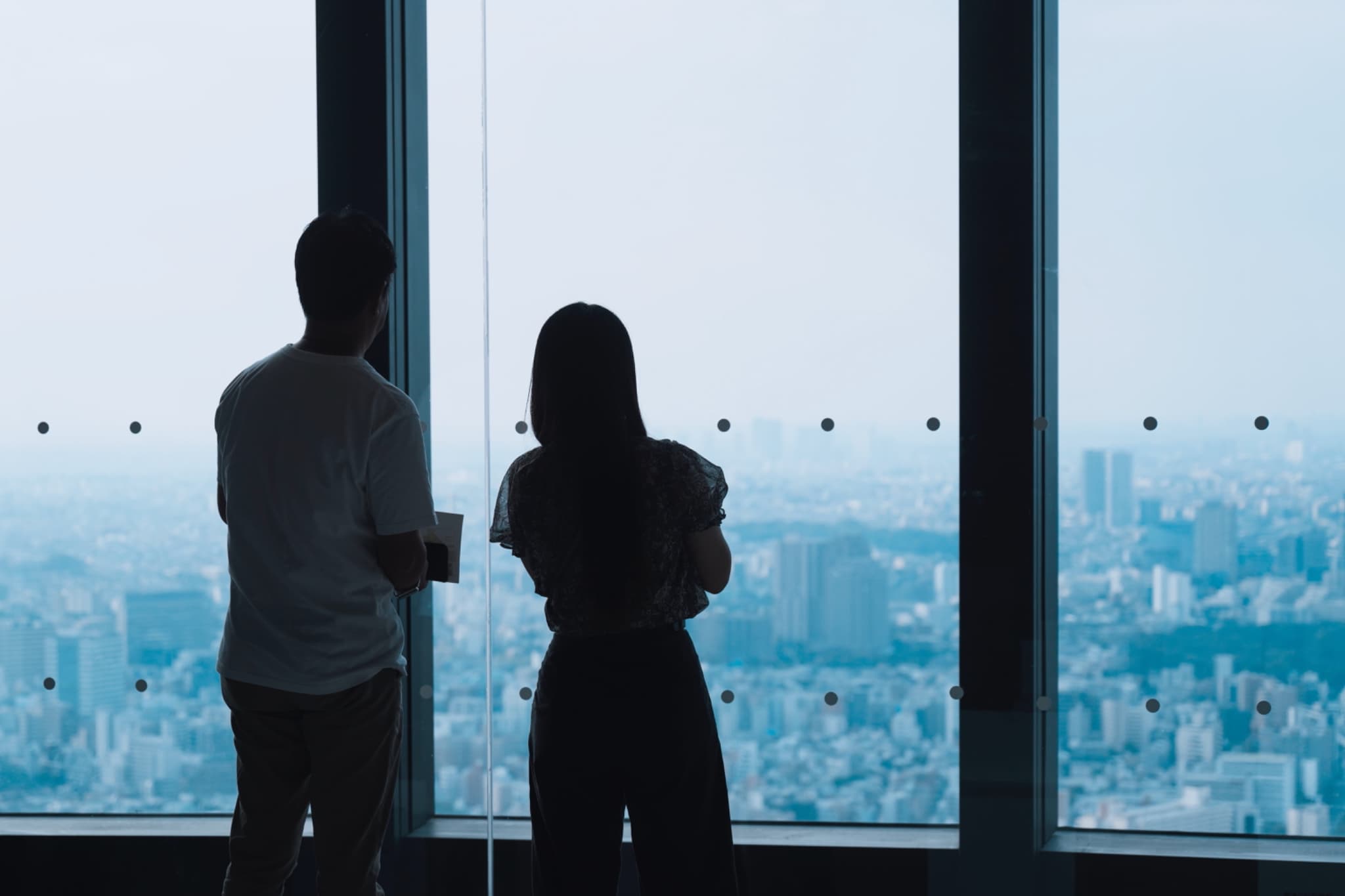 森美術館展示室で、窓の外の街並みを眺めている2人のシルエット。